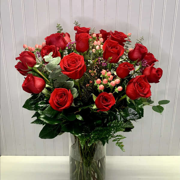 Tall arrangement of red roses with pink accent flowers in a clear glass vase