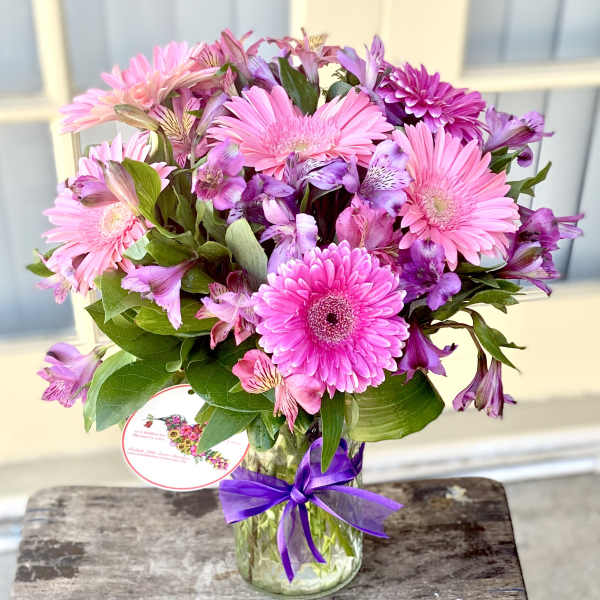 Pink and purple mixed bouquet in a glass vase with a purple ribbon