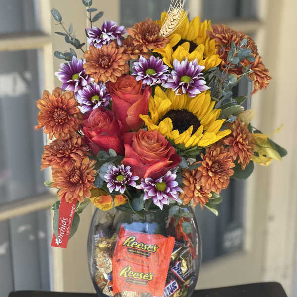 Mixed bouquet of roses, sunflowers, and chrysanthemums in a glass vase with candy