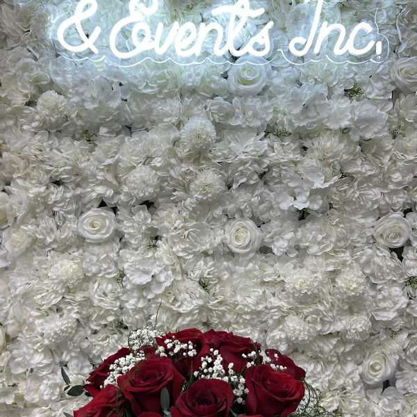 Red rose bouquet in front of a white floral wall with a glowing sign
