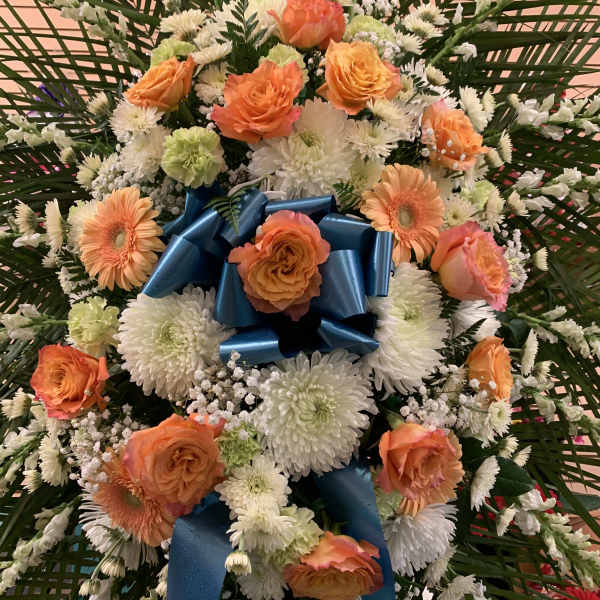 Orange roses and white daisies arranged with a blue ribbon bow