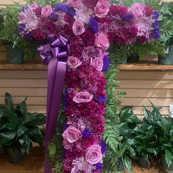 Large floral cross with pink and purple flowers and a ribbon bow
