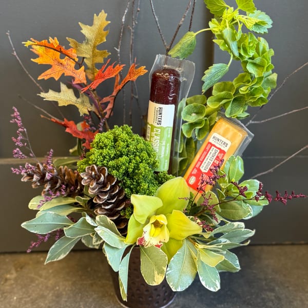 Autumn floral arrangement with an orchid, pinecones, and packaged candy bars in a vase.