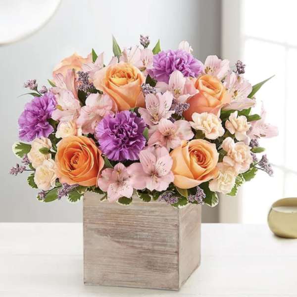 Bouquet of peach roses, pink flowers, and purple carnations in a wooden box