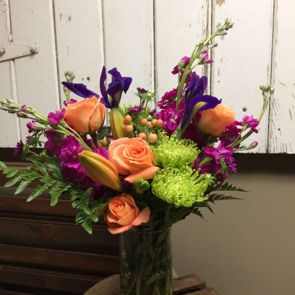 Colorful bouquet of orange roses, purple irises, and green chrysanthemums in a glass vase