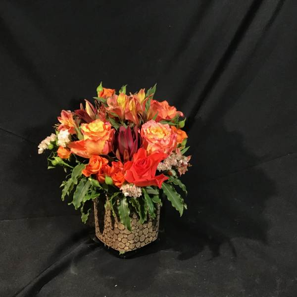 Orange and red mixed flower arrangement in a textured vase