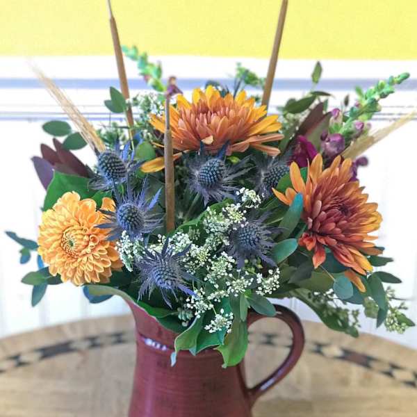 Mixed bouquet in a burgundy pitcher vase with orange and blue flowers