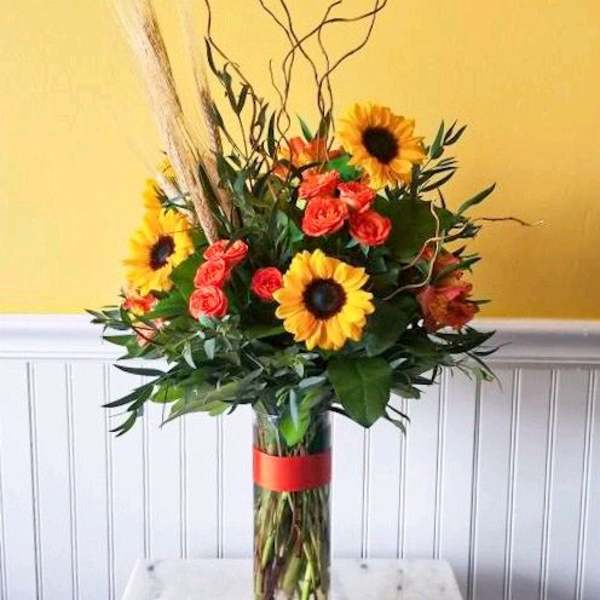Sunflower and rose arrangement in a tall glass vase with a red ribbon