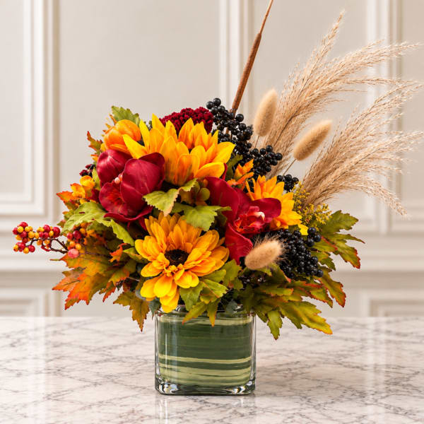 Autumn bouquet with yellow sunflowers, red blooms, and dried grasses in a glass vase