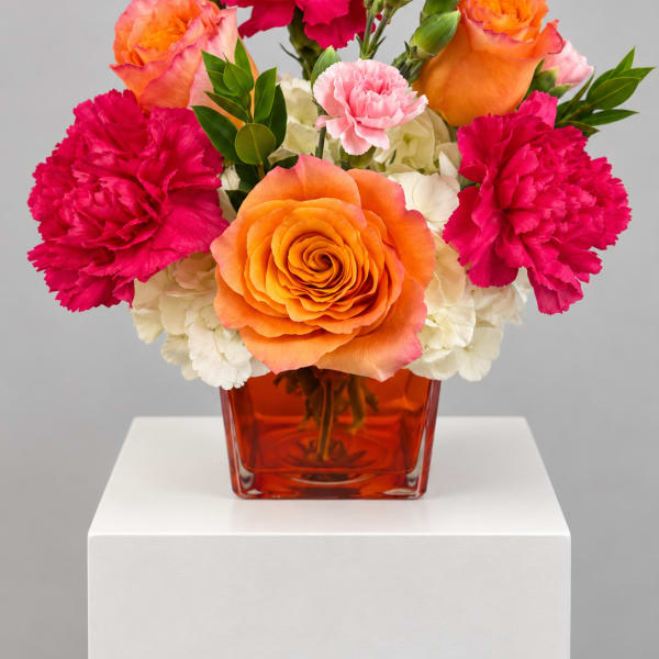 Orange roses and pink carnations in a red glass vase