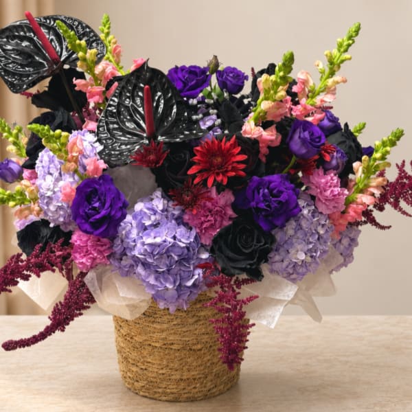 Purple and pink floral arrangement in a woven basket with black anthuriums