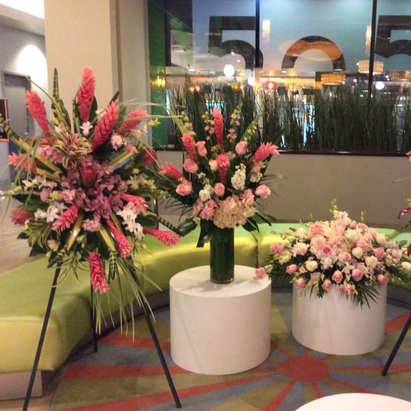 Four pink floral arrangements displayed on stands and pedestals in a lobby