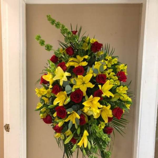 Standing floral spray with red roses and yellow lilies on a metal easel