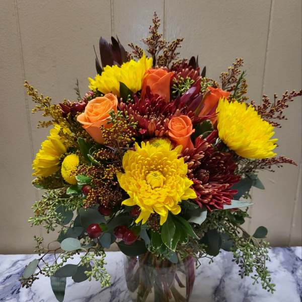 Mixed bouquet of yellow chrysanthemums and orange roses in a glass vase