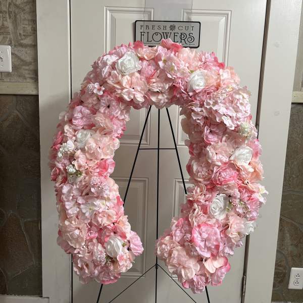 Pink and white floral wreath on a black stand