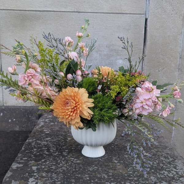 Pastel floral arrangement in a white pedestal vase with peach and pink blooms