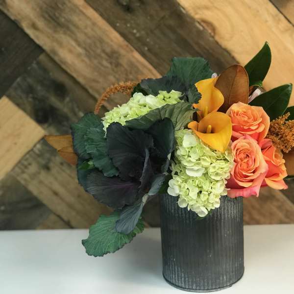 Arrangement of orange roses, yellow calla lilies, and green hydrangeas in a dark vase