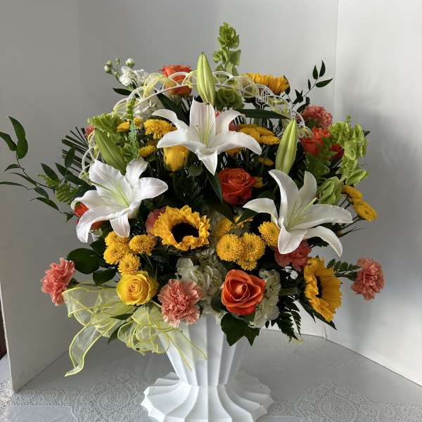 Large mixed bouquet with white lilies, roses, sunflowers, and carnations in a white vase