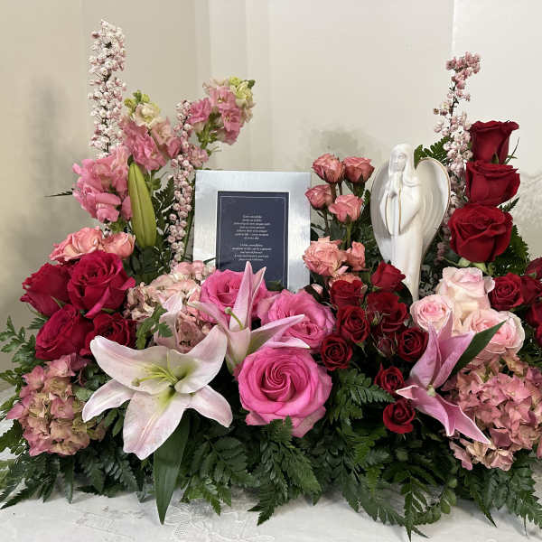 Large floral sympathy arrangement with pink and red roses, lilies, and an angel figurine