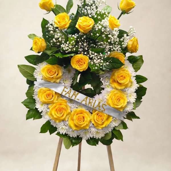Yellow rose wreath on an easel with white flowers and a ribbon
