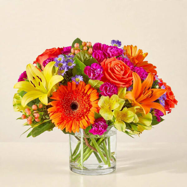 Bright mixed bouquet in a clear glass vase with orange, pink, yellow, and purple blooms