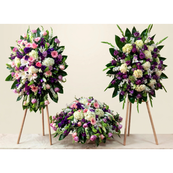 Three floral funeral arrangements in pink, purple, and white on stands and a low base