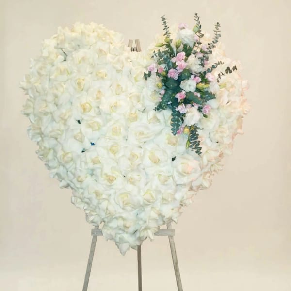 Heart-shaped white floral standing arrangement on an easel with pink accents