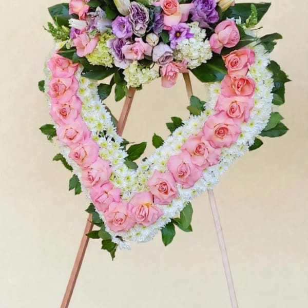 Heart-shaped floral wreath with pink roses and white flowers on a stand