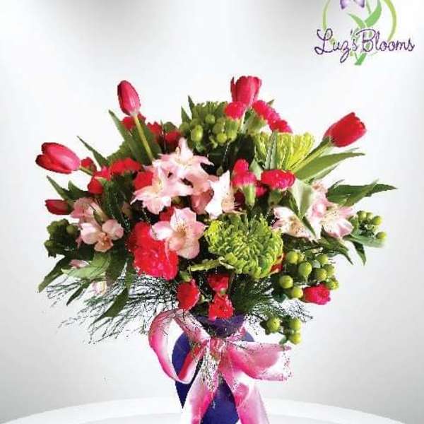Bouquet of red tulips and pink lilies in a purple vase with a pink ribbon