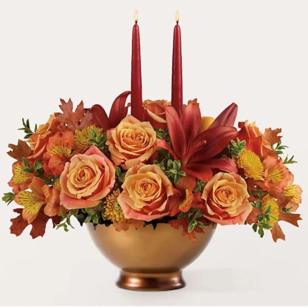 Autumn floral arrangement with roses in a gold bowl and two red taper candles