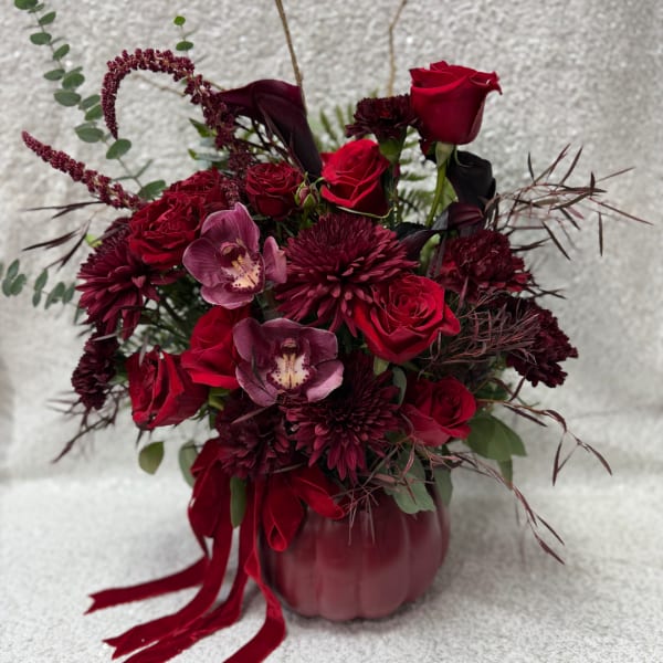 Red roses and burgundy flowers arranged in a pumpkin vase