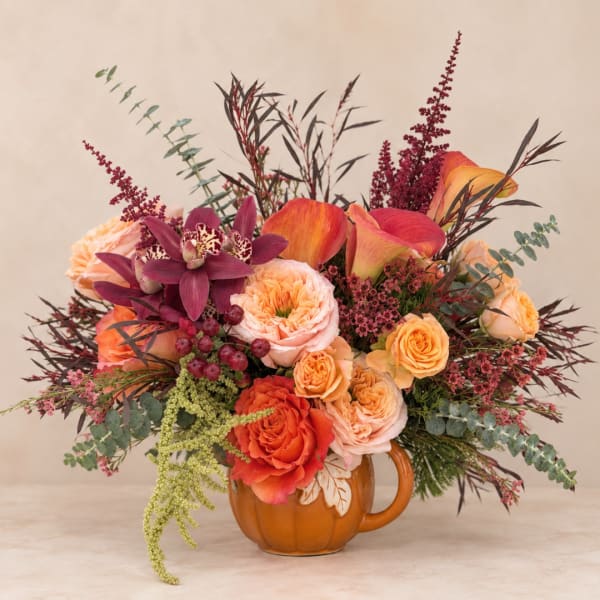 Autumn bouquet of roses, calla lilies, and orchids in a pumpkin mug