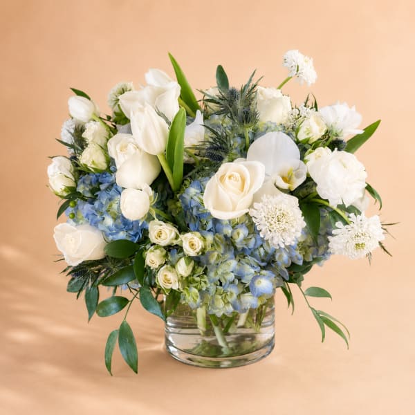 White roses and tulips with blue hydrangeas in a glass vase
