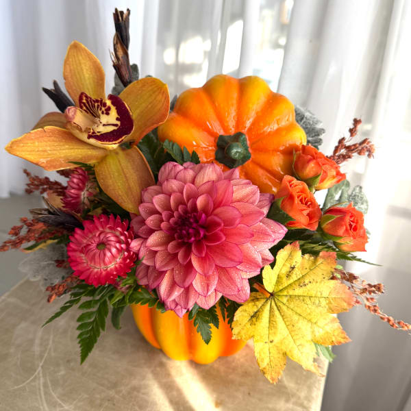 Autumn floral arrangement in a pumpkin-shaped container with pink and orange blooms