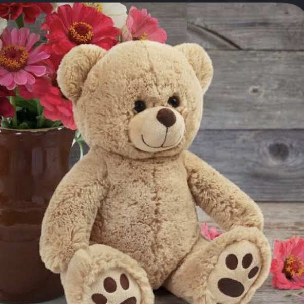 Teddy bear beside a vase of pink flowers