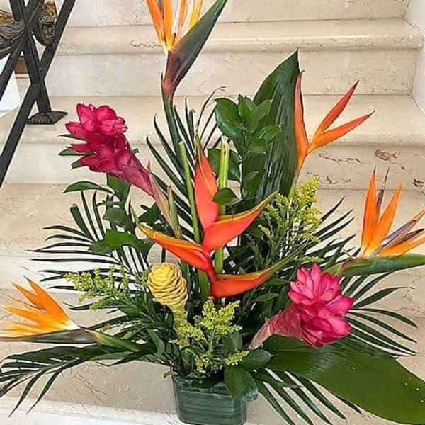 Tall tropical arrangement with orange and pink flowers and lush foliage in a low rectangular container