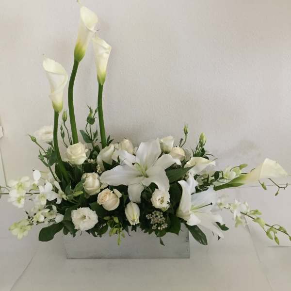 White floral arrangement with calla lilies, roses, and a lily in a rectangular vase