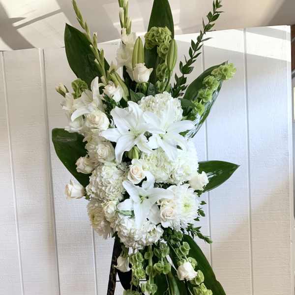Tall white floral standing spray on an easel with lilies and roses