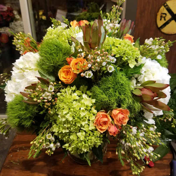 Large bouquet of orange roses, white hydrangeas, and green blooms in a glass vase