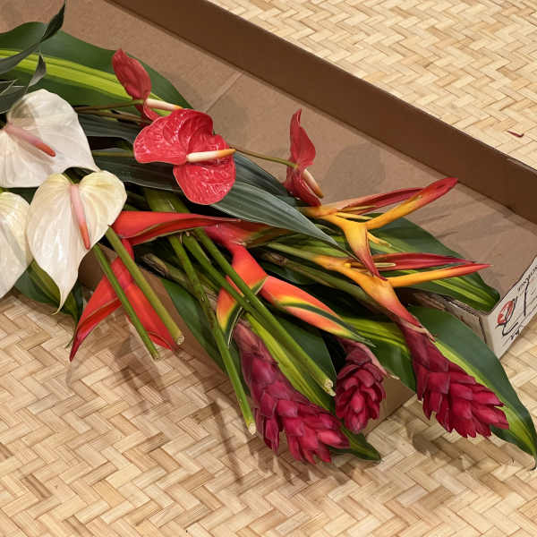 Bundle of assorted tropical flowers with large leaves laid in a cardboard box.