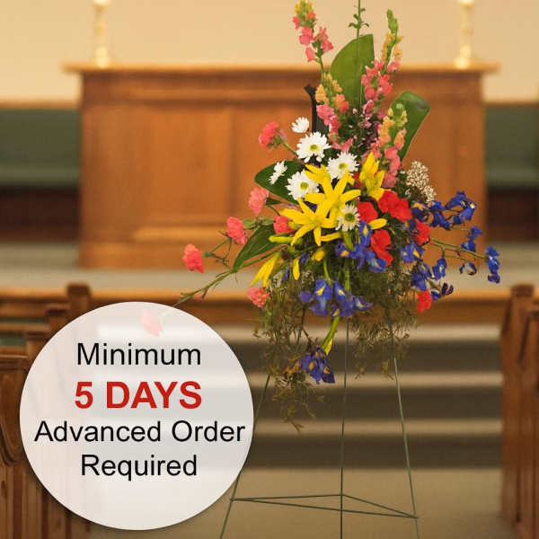 Tall multicolored standing spray with yellow lilies and mixed flowers on an easel in a church.