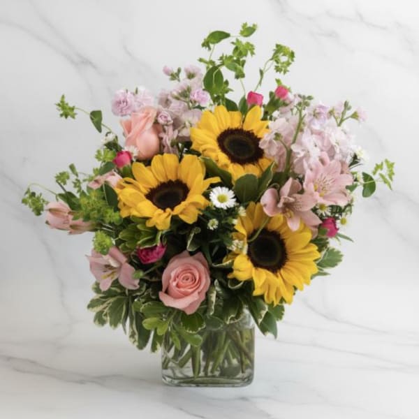 Mixed bouquet with sunflowers, pink roses, and pale pink blooms in a glass vase