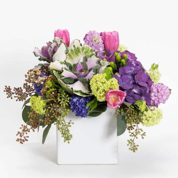 Colorful bouquet in a white square vase with pink, purple, and green blooms