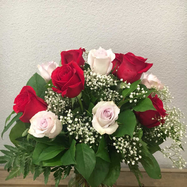 Arrangement of red and pale pink roses with white filler flowers in a clear glass vase on a wooden surface