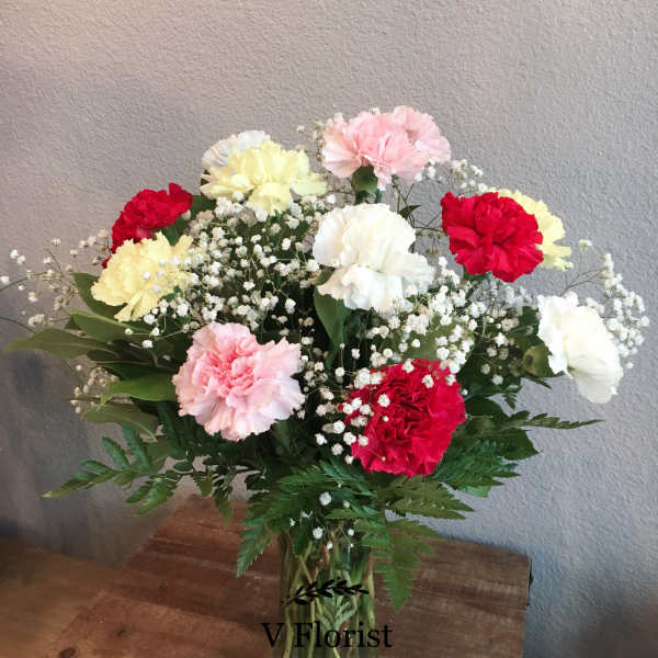 Mixed red, pink, white, and yellow carnations with baby's breath in a clear glass vase