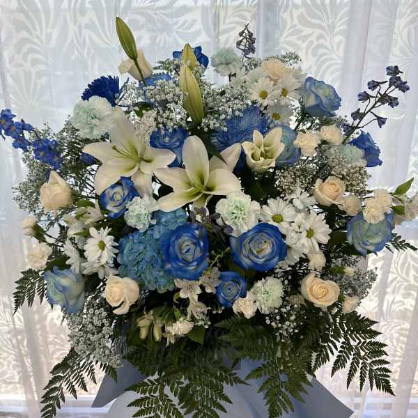 Tall blue and white standing flower arrangement with lilies, roses, and daisies on a tripod stand