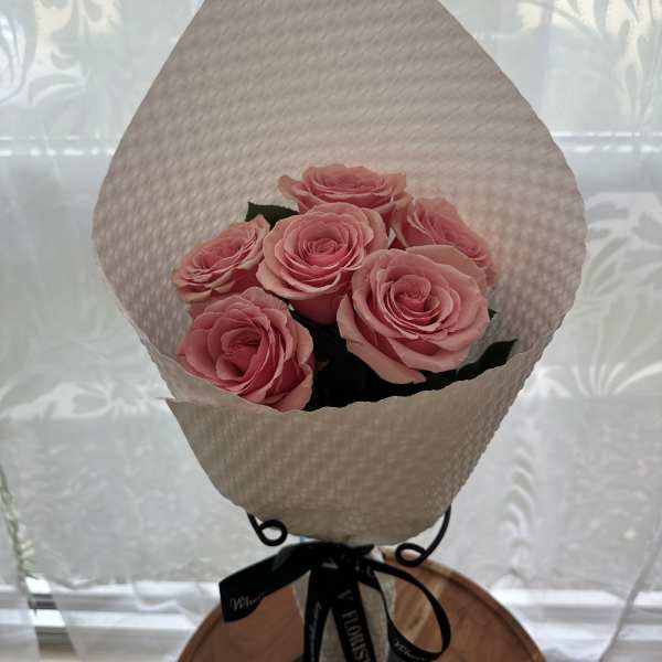 Small bouquet of pink roses wrapped in textured white paper with a black ribbon.