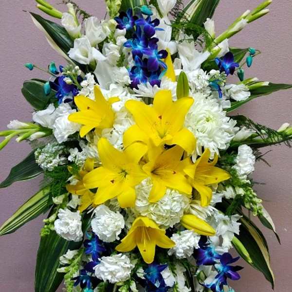 Tall floral standing spray with yellow lilies, white blooms, and blue orchids