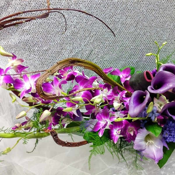 Long modern centerpiece of purple calla lilies and orchids with curved vine accents
