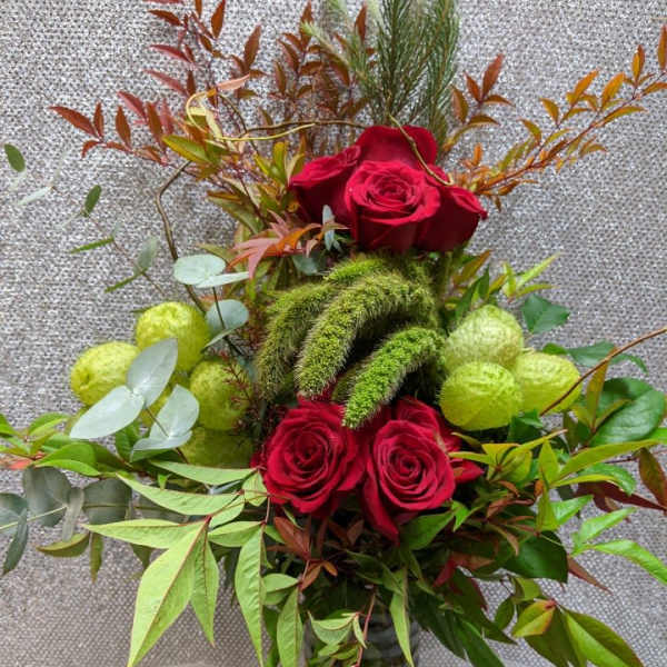 Red roses arranged in a glass vase with mixed greenery and green fuzzy accents